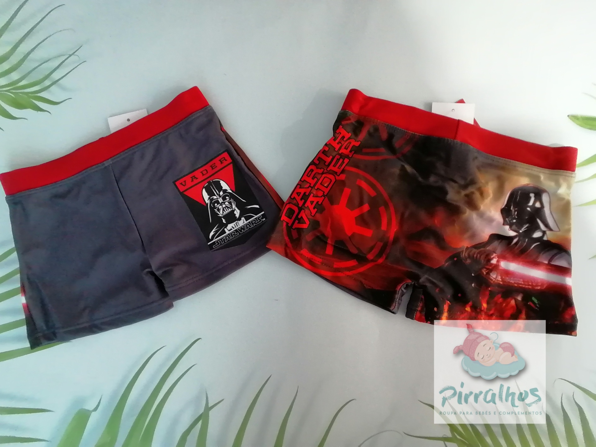 Dois boxers infantis Star Wars com cintura vermelha e estampas distintas colocados sobre superfície branca com plantas