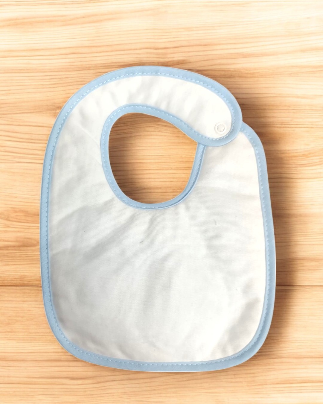 Babete branco com bordas azuis sobre madeira clara