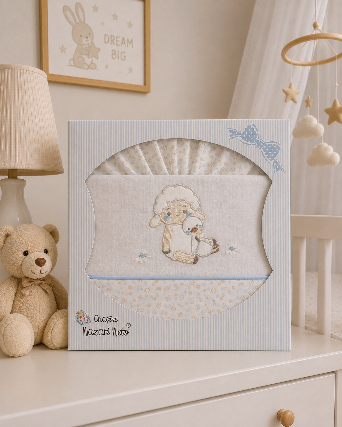 Conjunto de tecido para bebé com bordado de ovelha e pato numa caixa azul claro sobre uma cômoda branca com abajur e peluche.