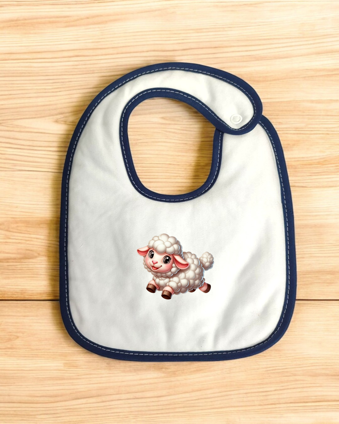 Babete branco com bordas azuis e desenho de cordeiro sobre fundo de madeira