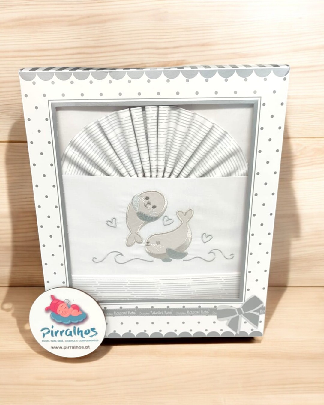 Conjunto de roupa de bebé branca com golfinhos cinza numa embalagem decorada com pontos cinza.