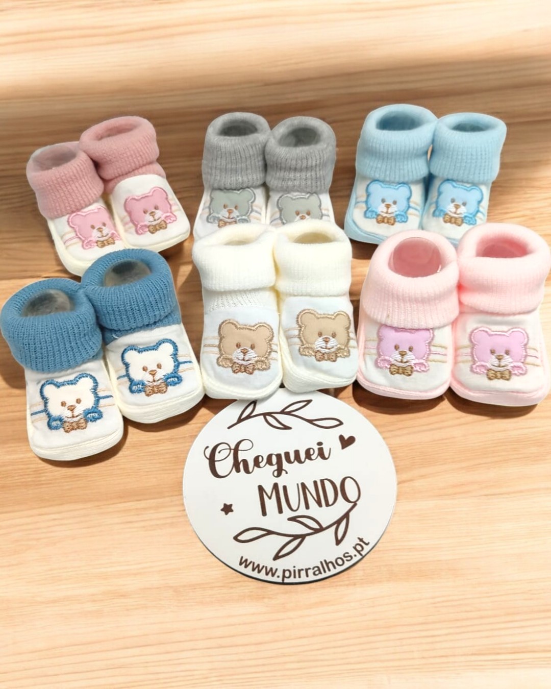 Seis pares de sapatinhos de bebé em várias cores com ursinhos bordados e cartão com texto CHEGUEI MUNDO