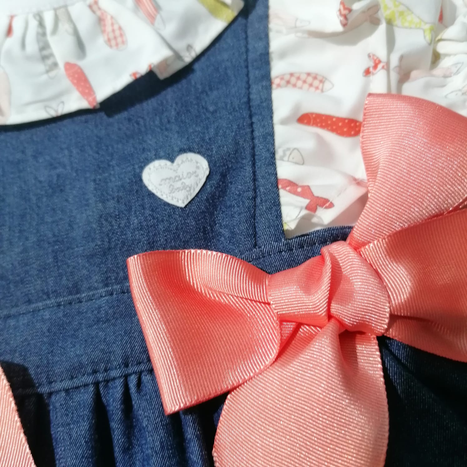 Vestido infantil com tecido azul tipo ganga, parte superior branca com peixinhos rosa e vermelho e laço rosa salmão.