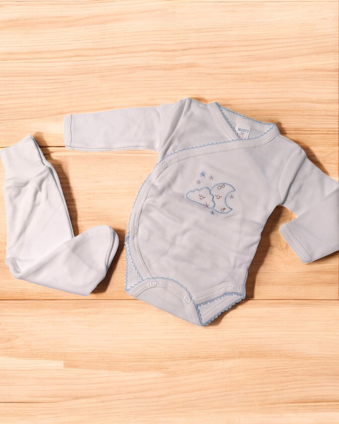 Conjunto de body e calças de bebé azul claro com bordado de lua e estrelas sobre madeira clara