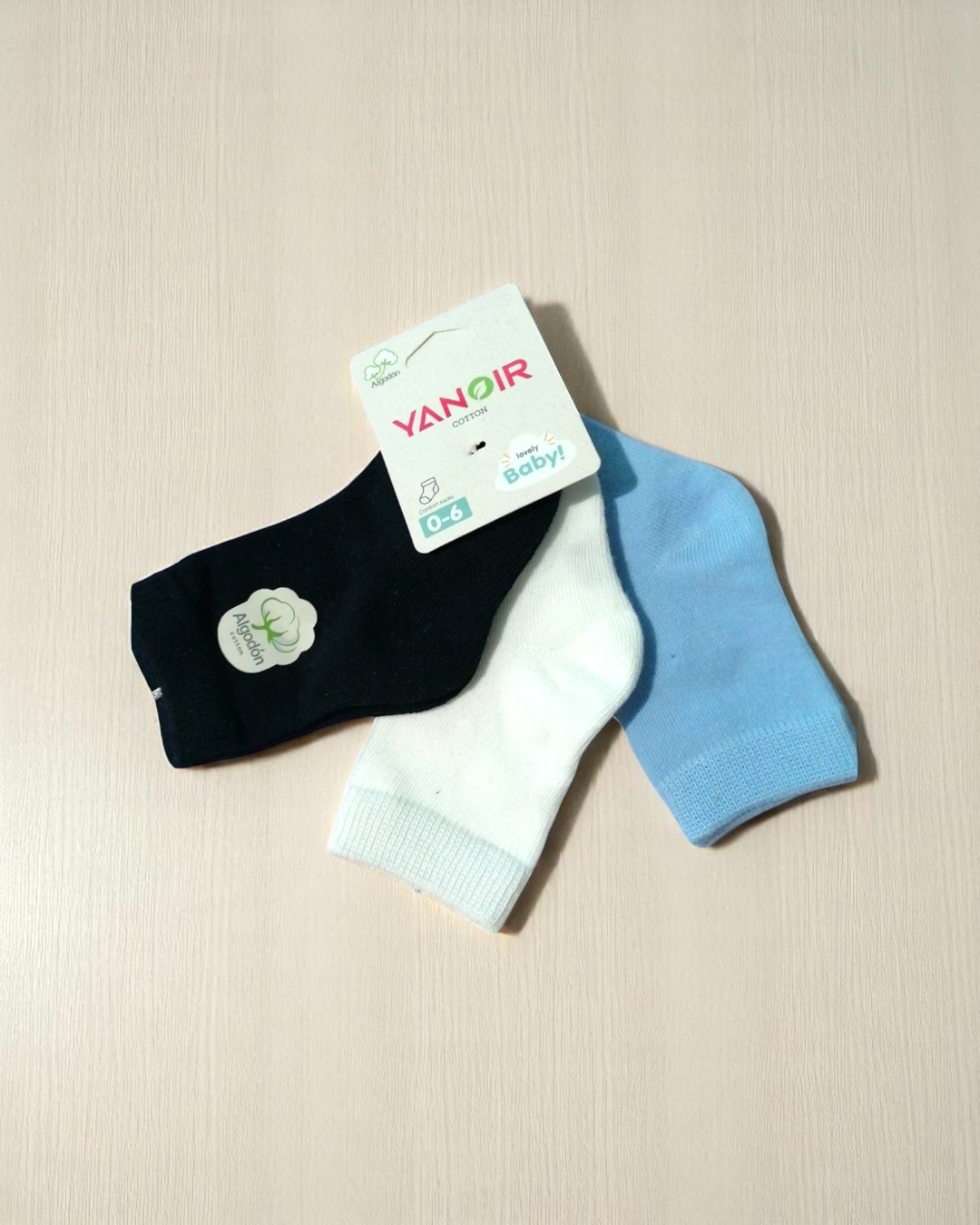 Três pares de meias para bebé nas cores preta, branca e azul clara com etiqueta YANOIR 0-6