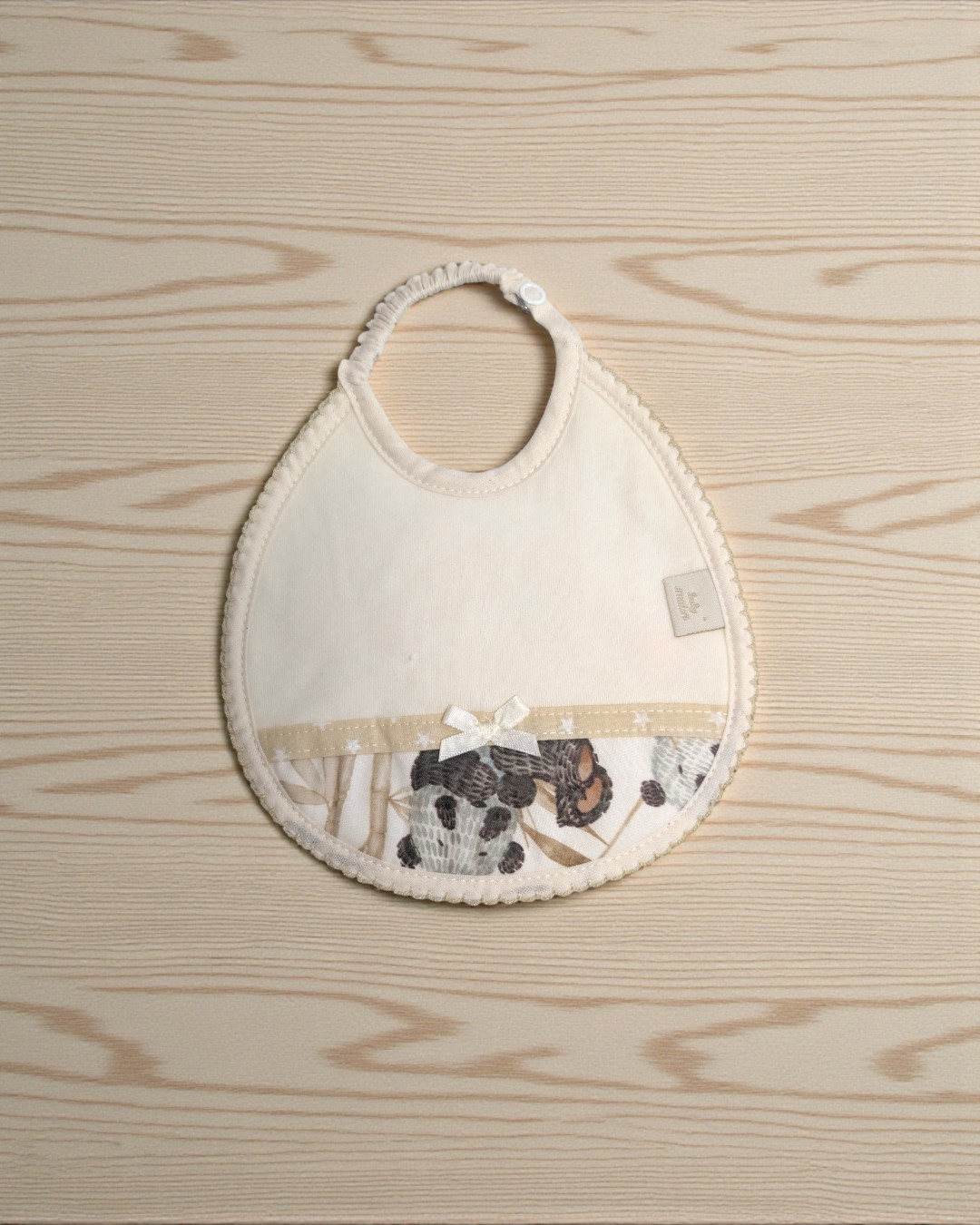 Babete de bebé bege com padrão floral cinza e castanho e laço branco