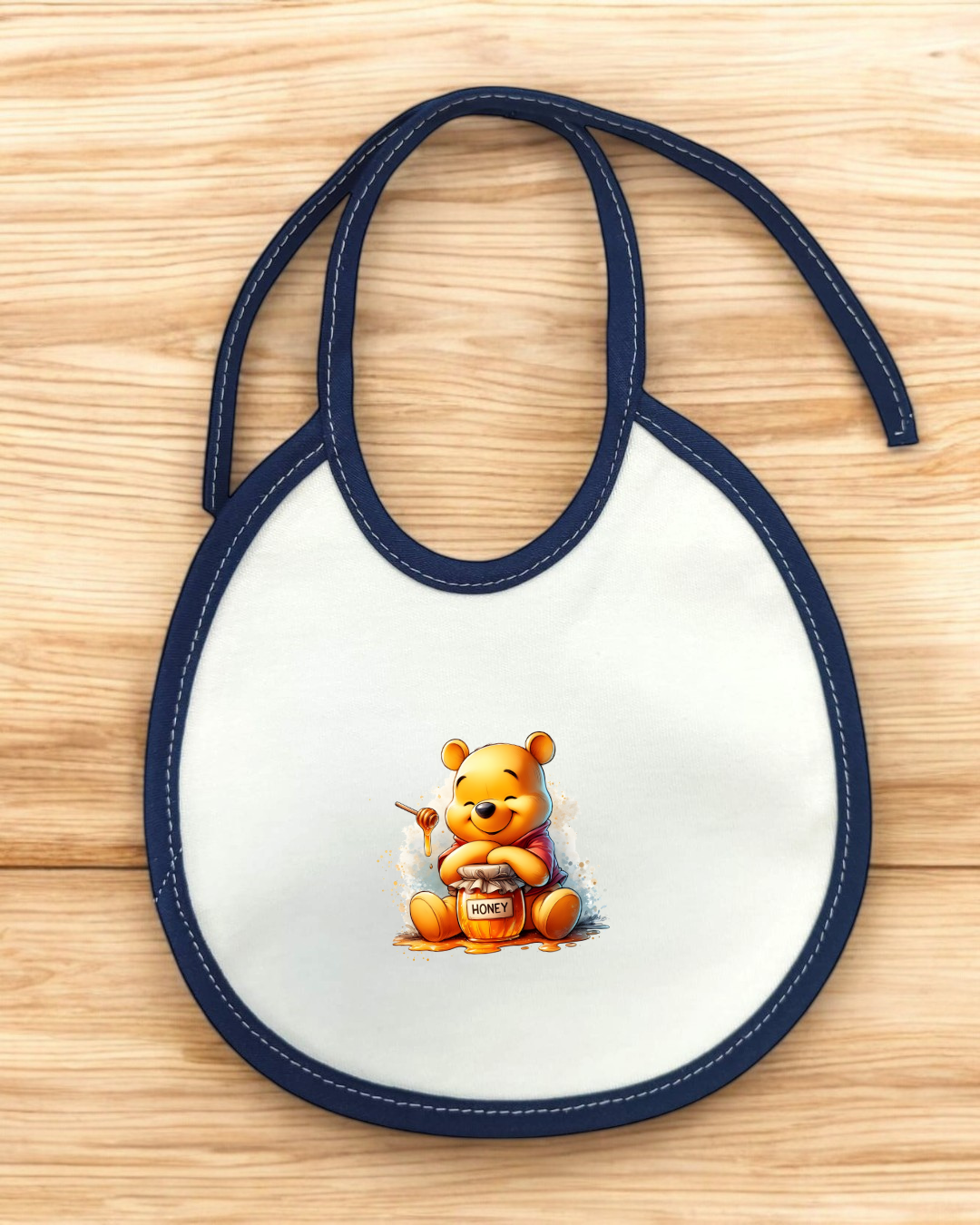 Babete branco e azul com desenho de ursinho amarelo a segurar pote de mel