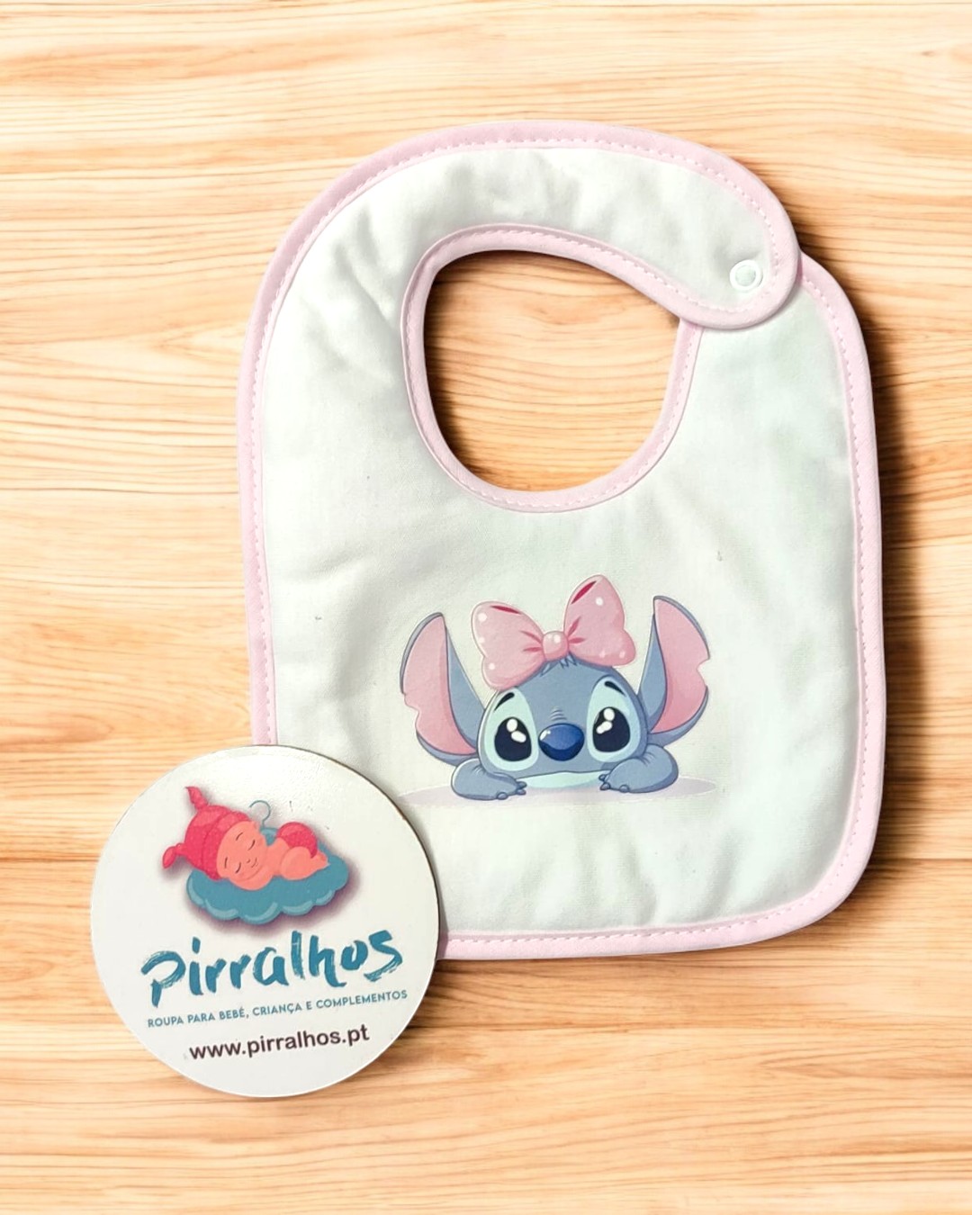 Babete de bebé branco com borda rosa e personagem azul com laço rosa