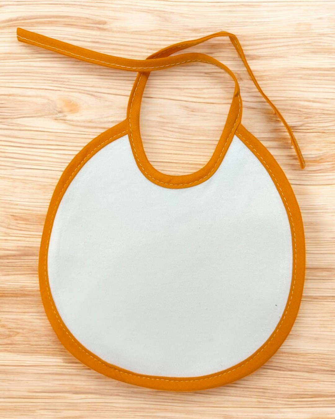 Babete redondo bege com rebordo e cordão laranja sobre madeira clara