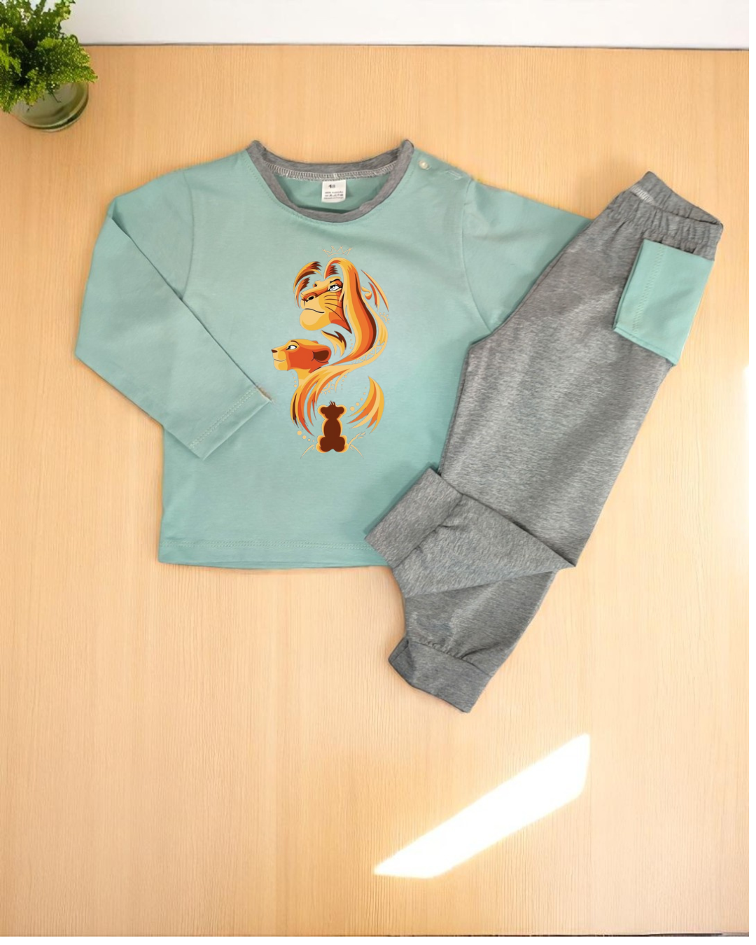 Conjunto de roupa de criança com camisola azul-pistácio e calças cinzentas sobre superfície de madeira