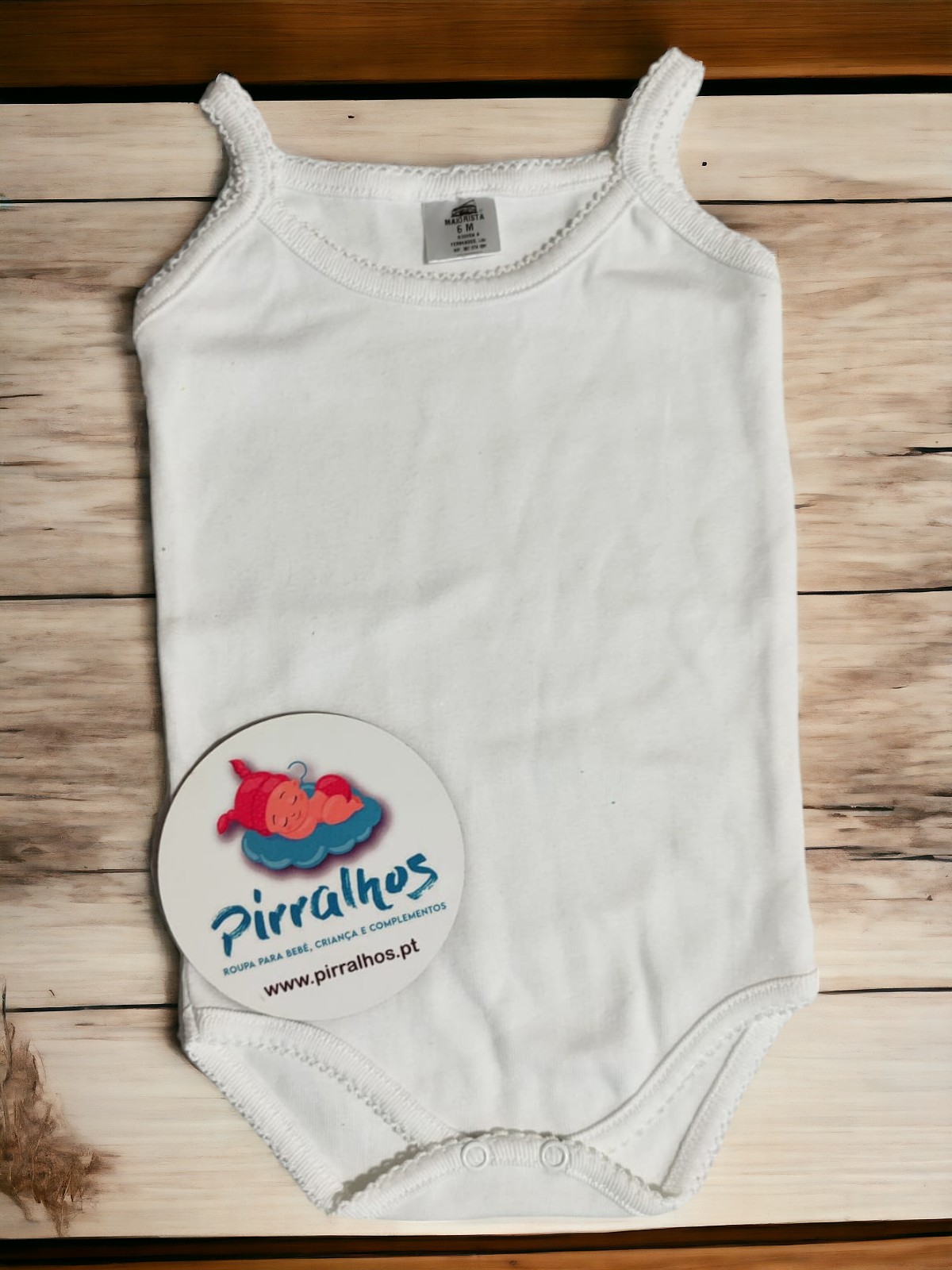 Body branco de bebé com alças finas e acabamento em crochê, com etiqueta interna e cartão redondo de identificação