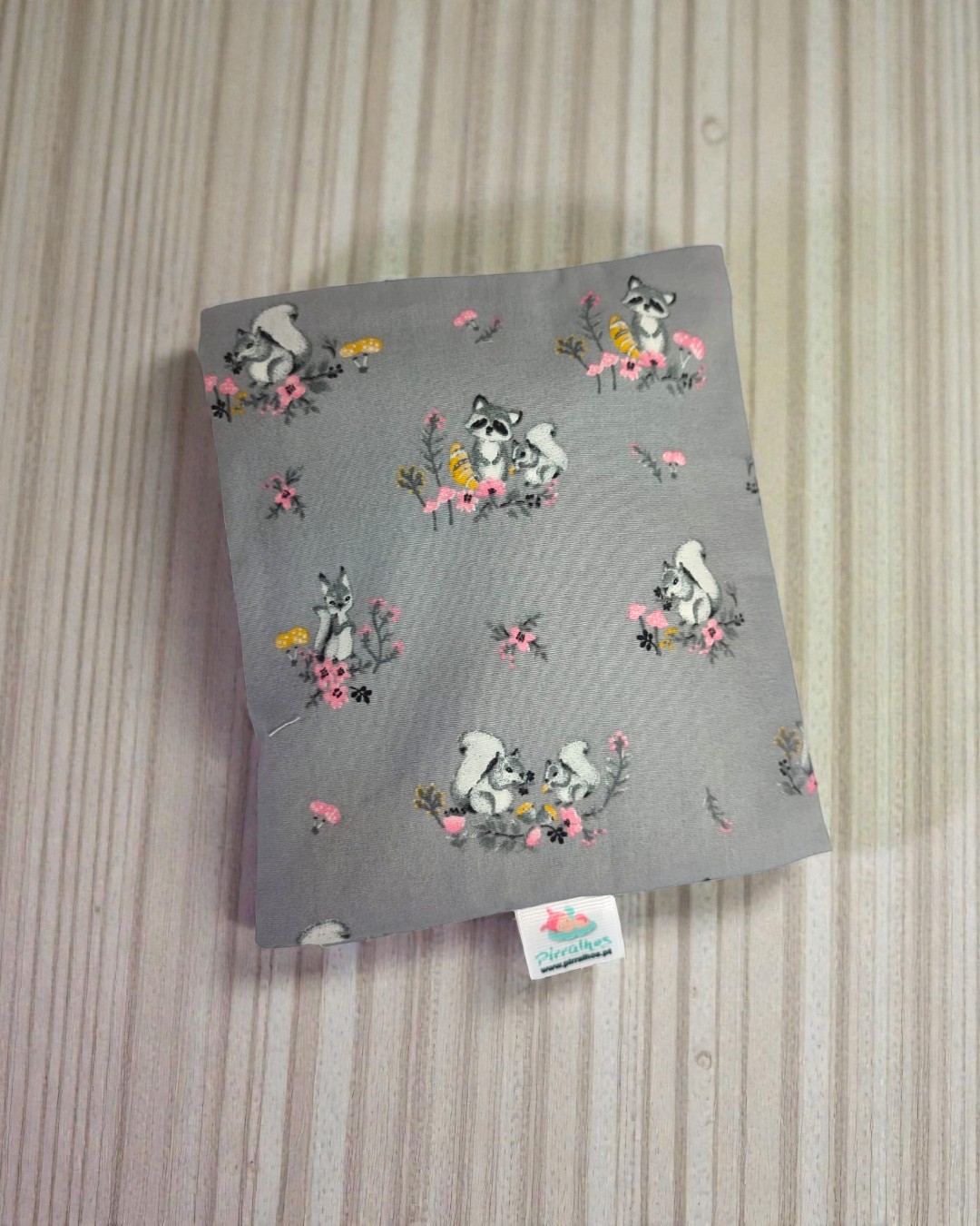 Tecido cinza com padrão de esquilos e flores cor de rosa e amarelas com etiqueta