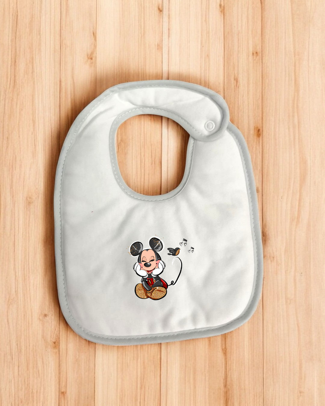 Babete branco com borda cinza e estampa de Mickey Mouse sentado com notas musicais.