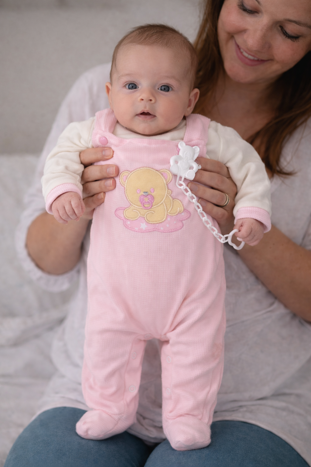 Bebé com macacão cor-de-rosa com urso bordado e chupeta branca com clipe em forma de urso