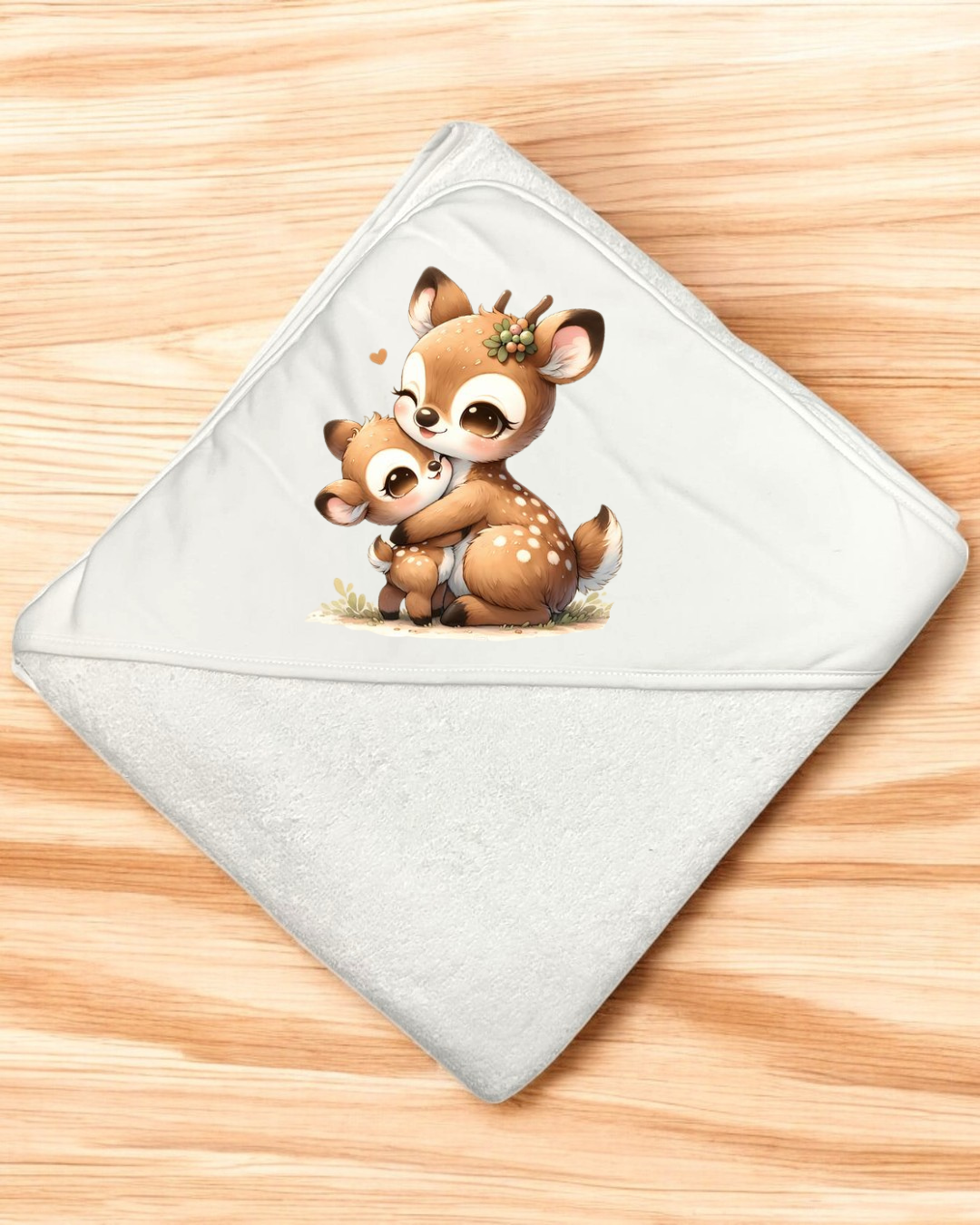 Toalha branca com capuz e desenho de dois veados castanhos abraçados sobre fundo de madeira