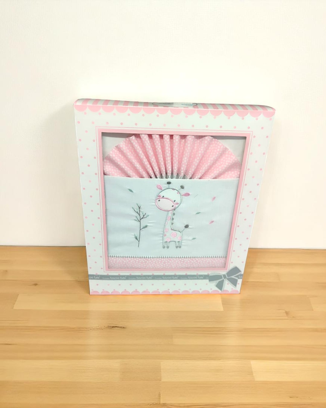 Produto têxtil para bebé com imagem de girafa dentro de caixa branca com detalhes cor-de-rosa
