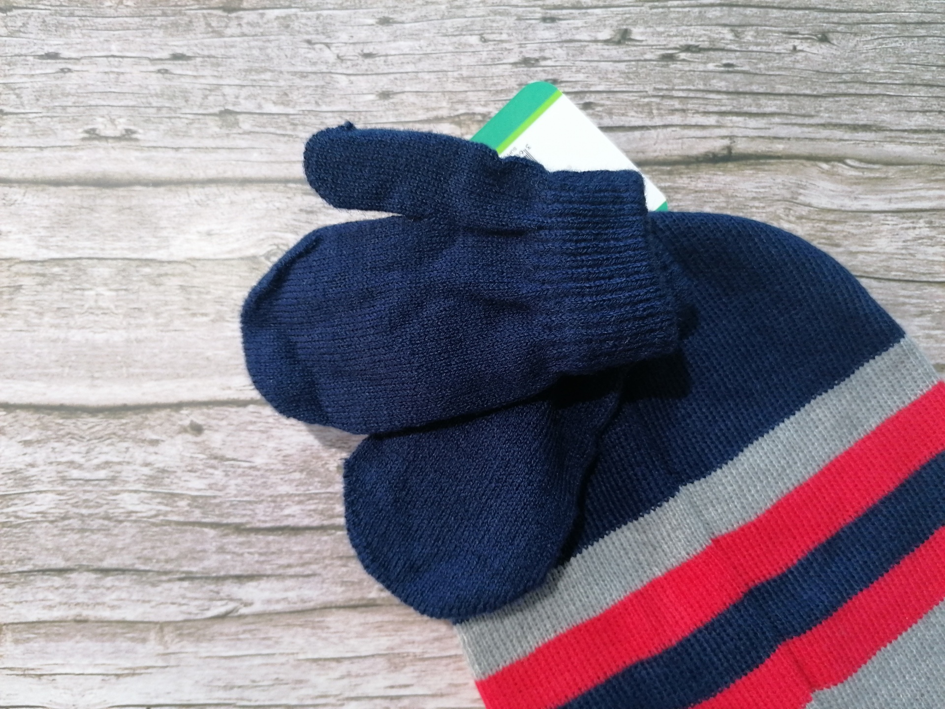 Luvas e gorro de malha azul escuro com riscas, sobre madeira clara