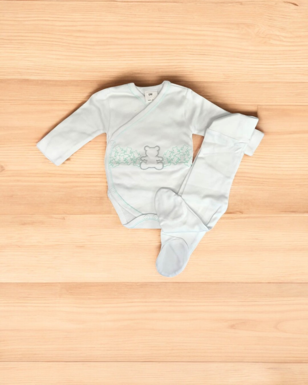 Conjunto de bebé branco com ursinhos verdes e cinzentos sobre madeira clara