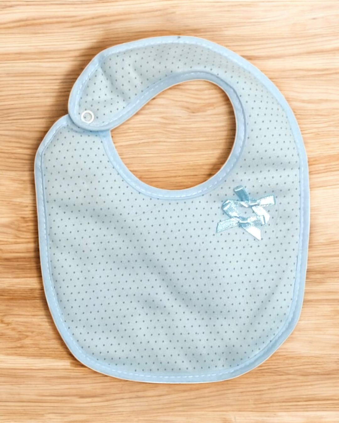 Babete azul claro com pontos pequenos escuros e laço