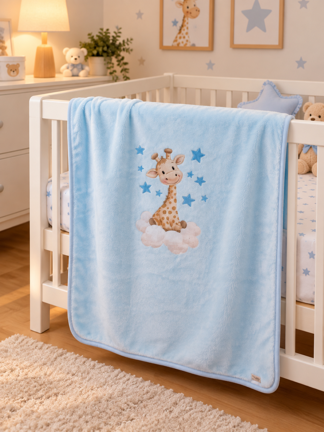 Manta azul clara com estampa de girafa sentada em nuvem num berço branco num quarto infantil.