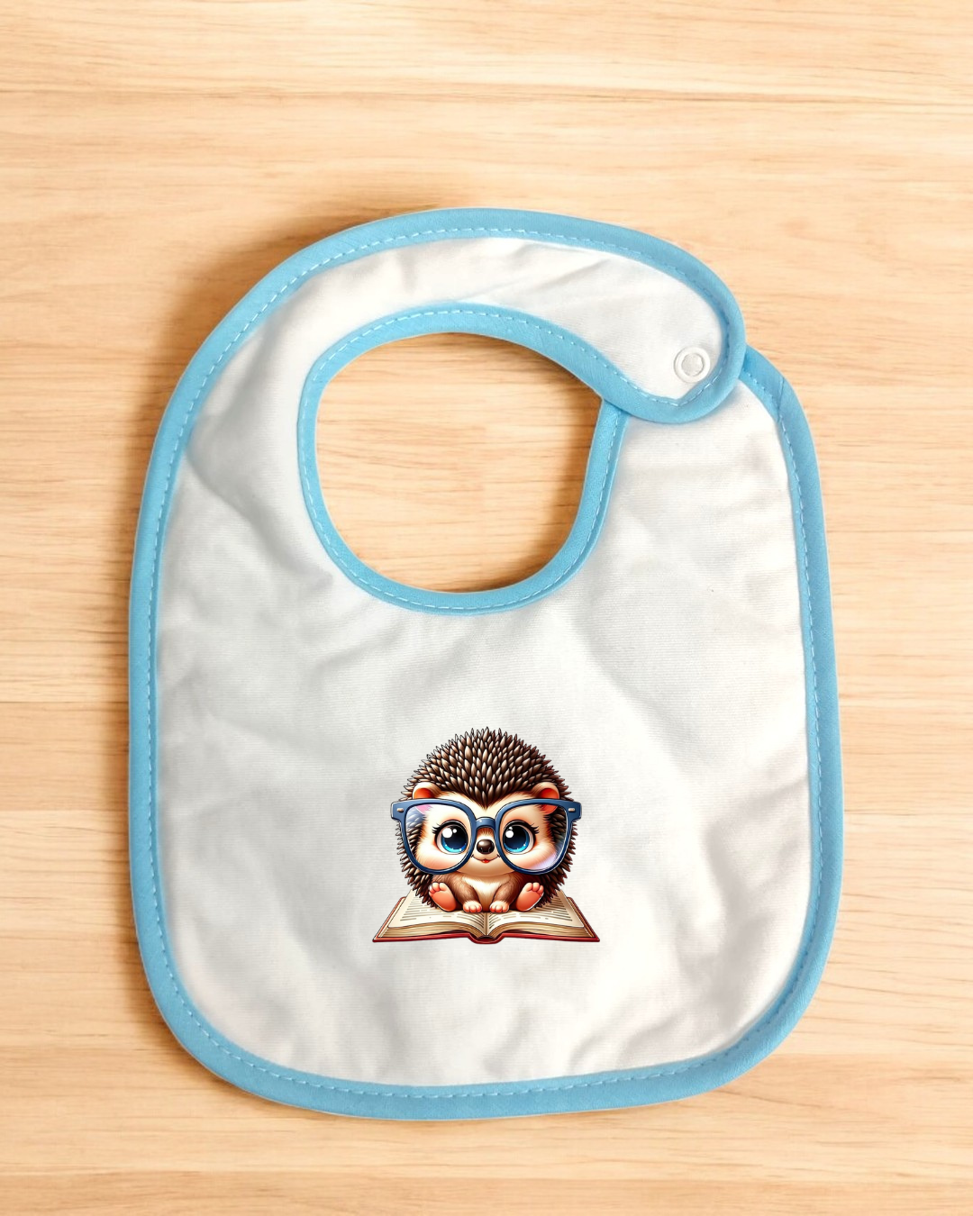 Babete branco com bordas azuis e estampa de ouriço com óculos sentado num livro