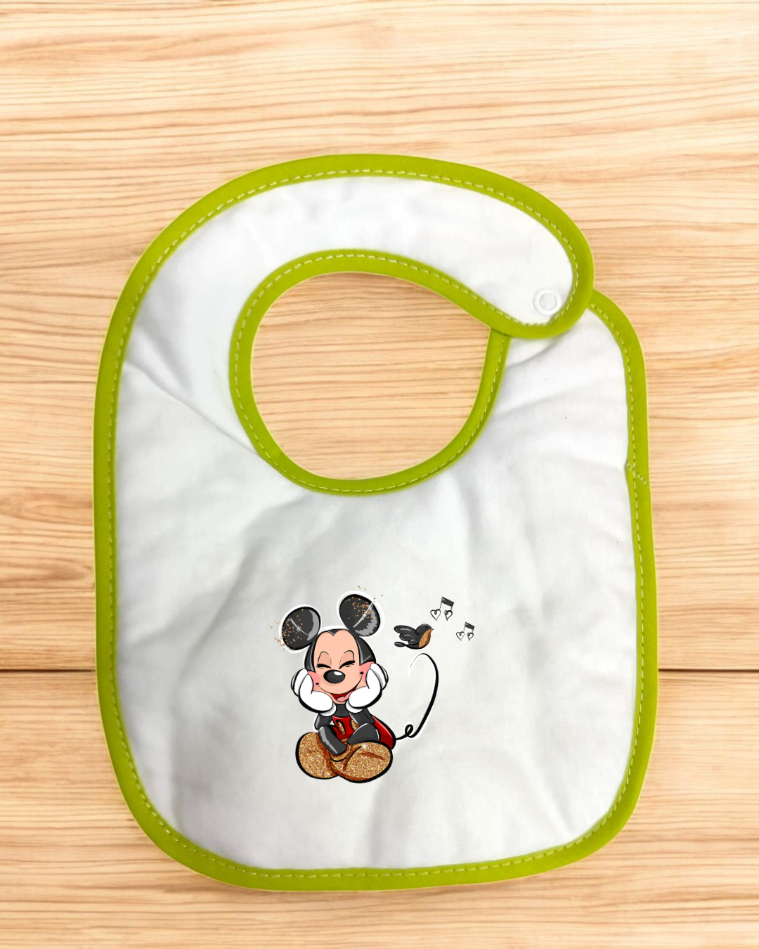 Babete de bebé branco com borda verde e imagem do Mickey Mouse sentado a ouvir música