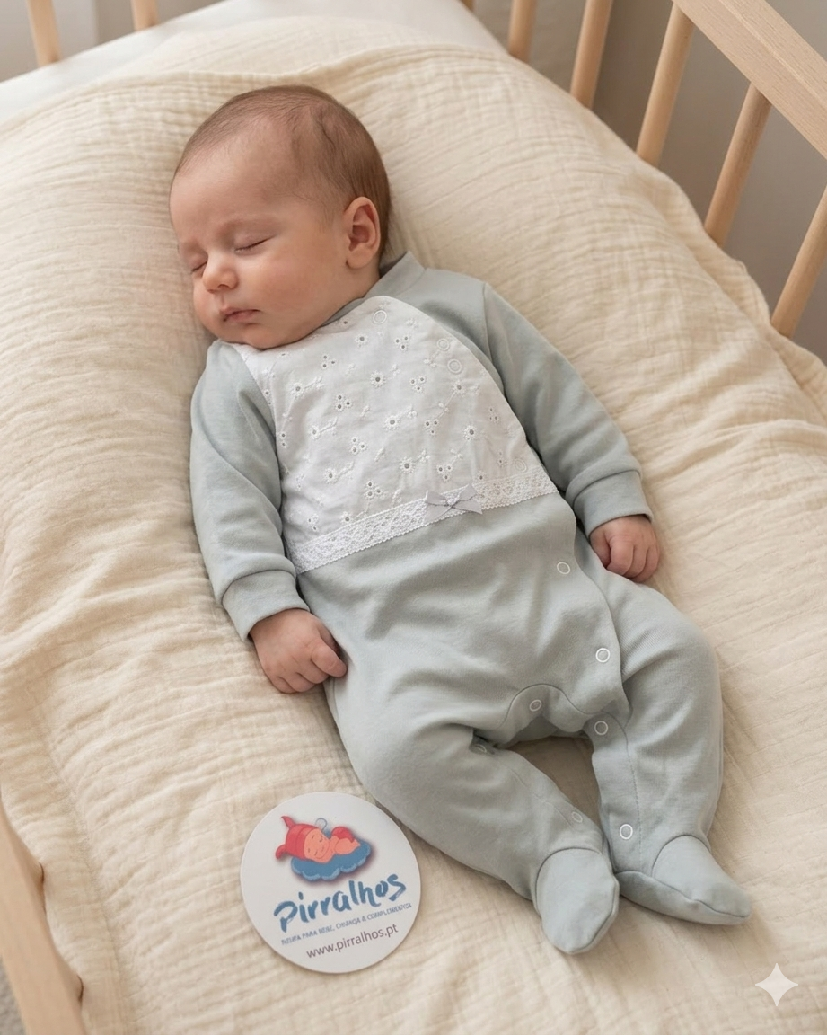 Bebé adormecido com fato cinzento com bordado branco deitado em almofada creme dentro de berço de madeira