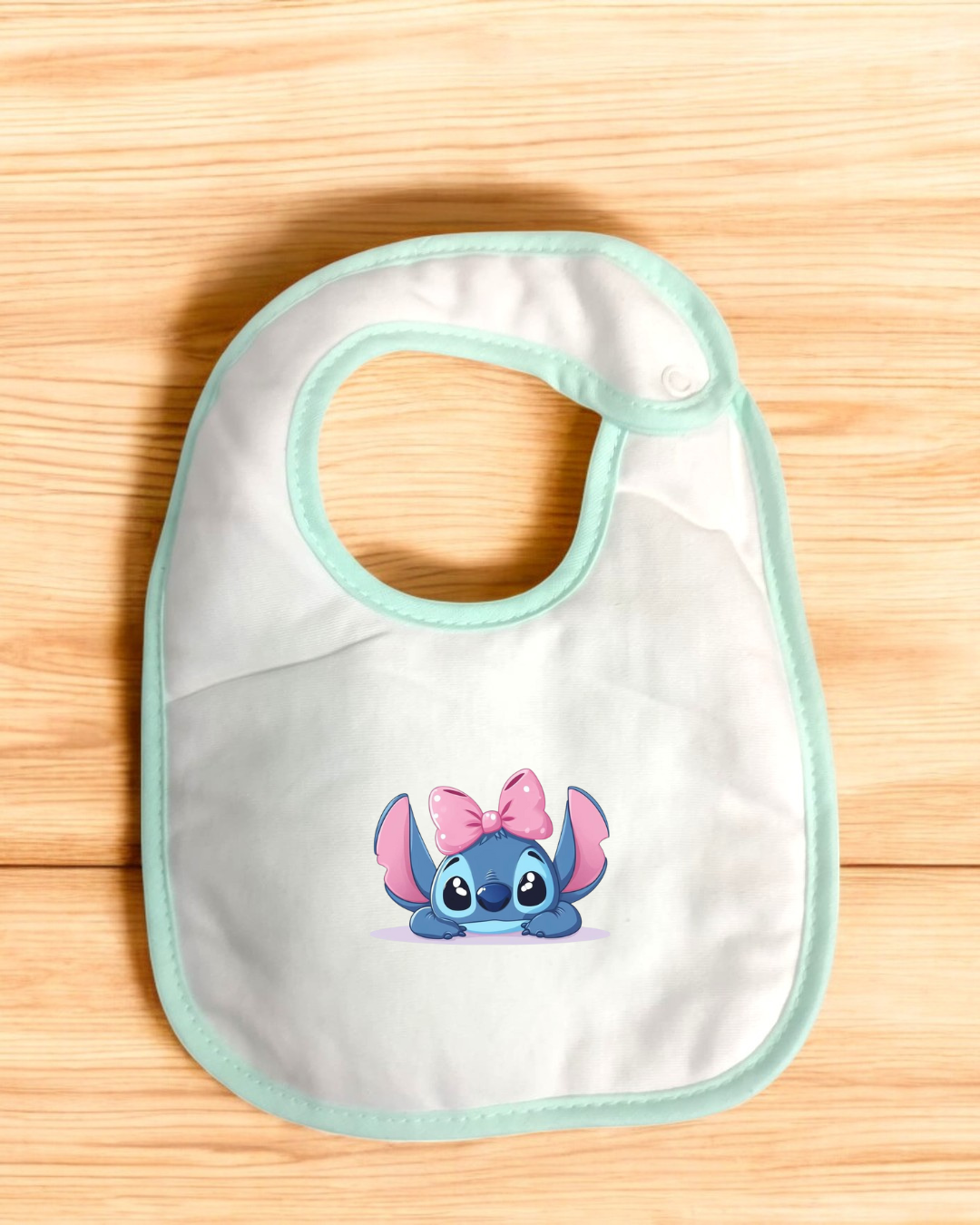 Babete branco com borda verde água e personagem azul com laço cor-de-rosa