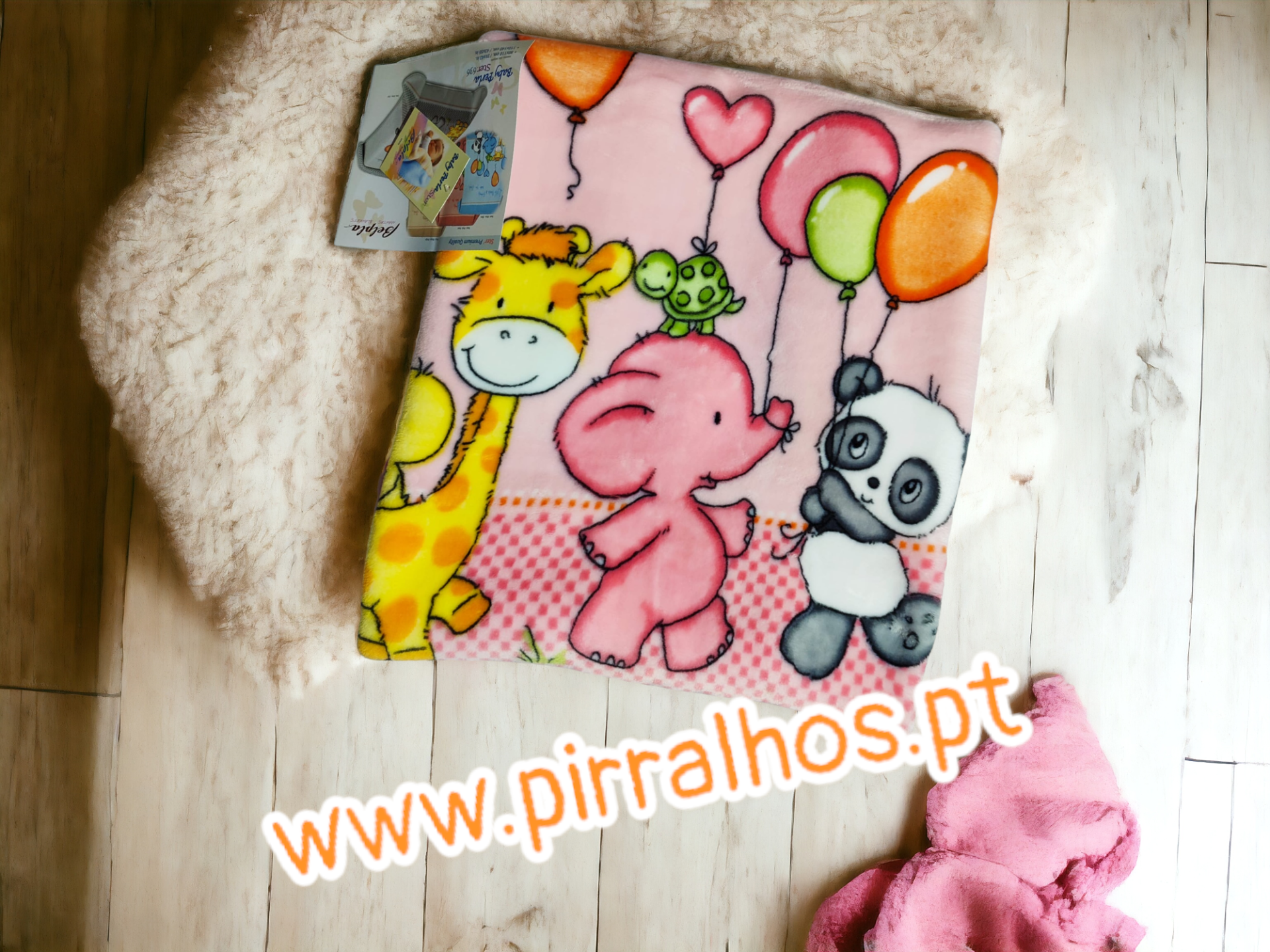 Cobertor infantil rosa com animais e balões coloridos sobre tapete e chão de madeira
