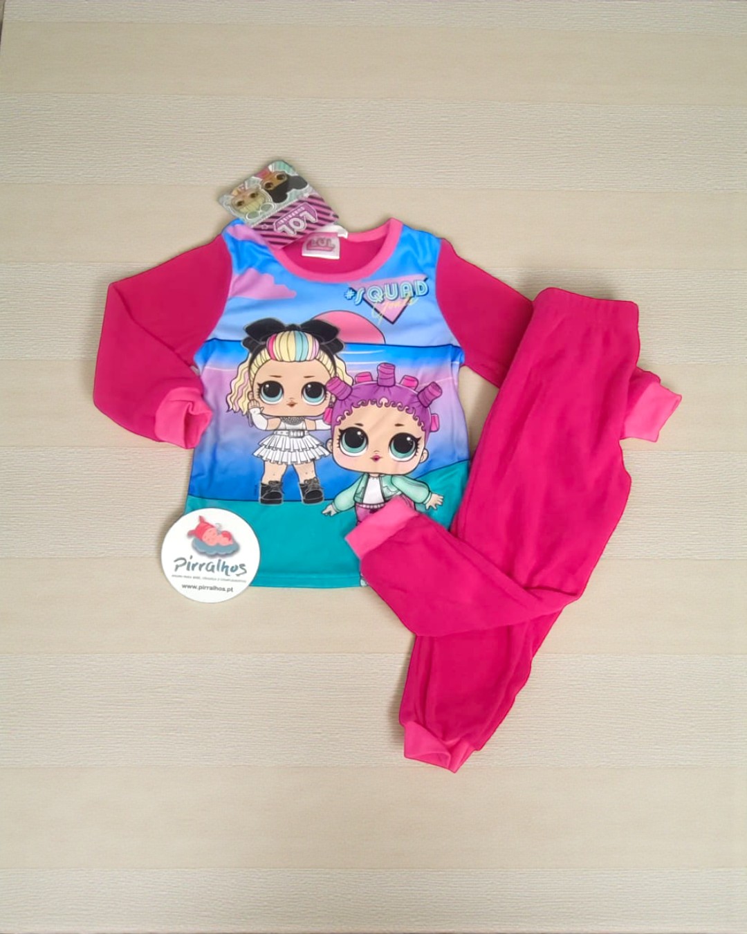 Conjunto de pijama infantil com estampa colorida e calças cor-de-rosa sobre superfície de madeira clara.