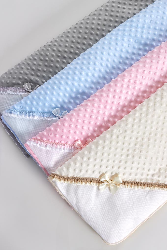 Fronhas de almofada texturizadas em cinza, azul, rosa e branco com laços decorativos.