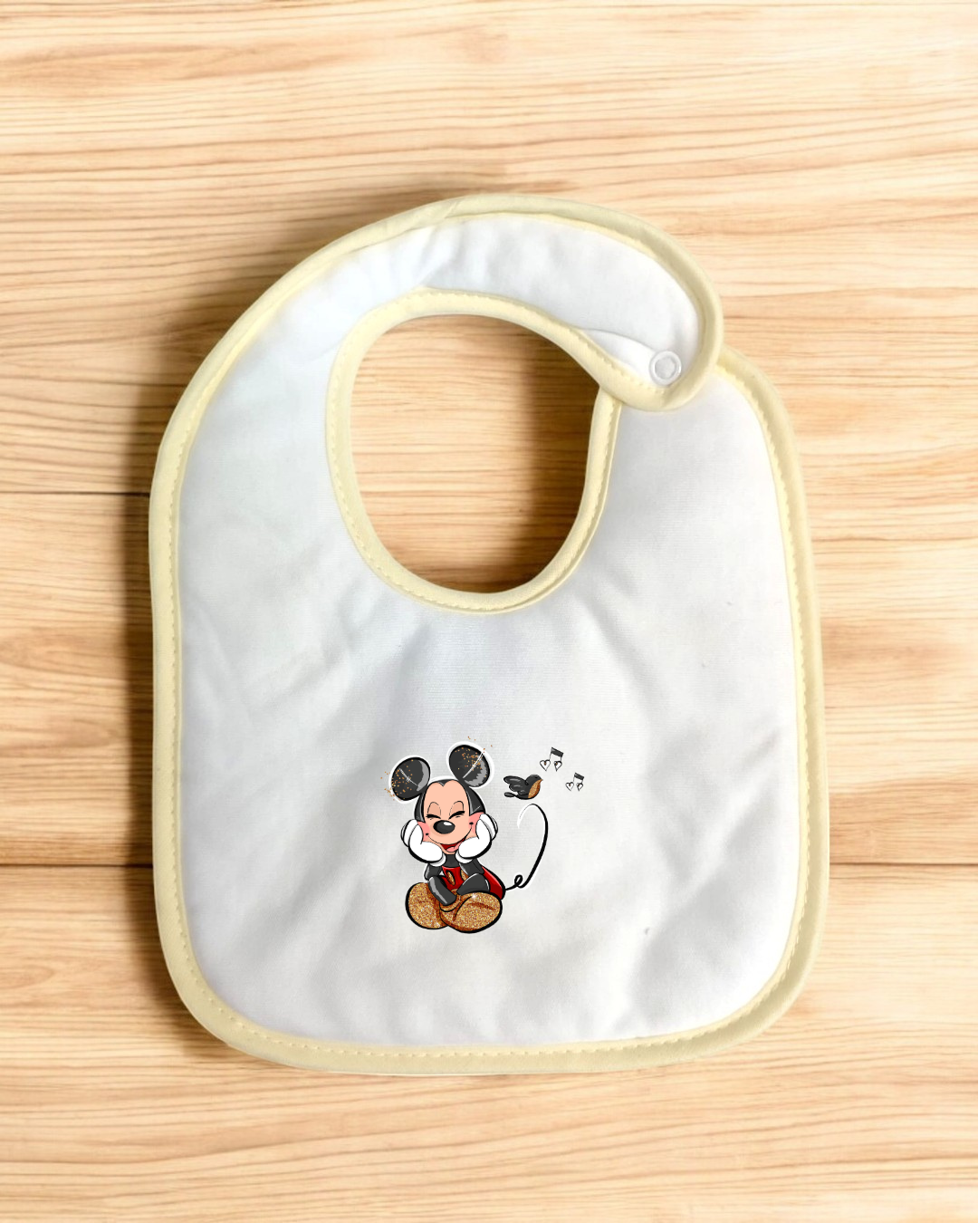 Babete branco com bordas amarelas e estampa do Mickey Mouse cantando.