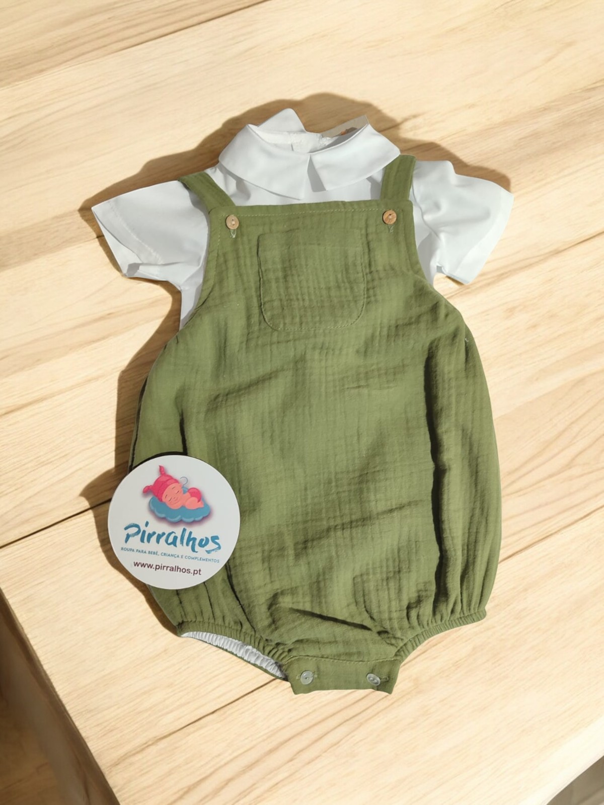 Macacão verde com body branco para bebé sobre madeira clara e etiqueta Pirralhos