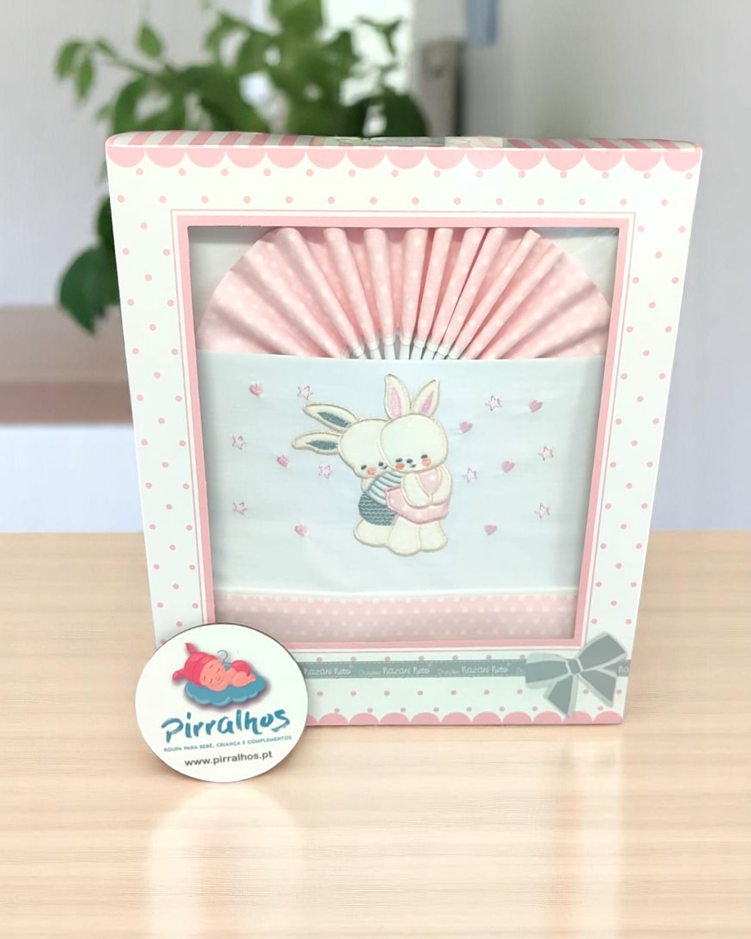Caixa branca e rosa com babetes decorados com coelhos abraçados.