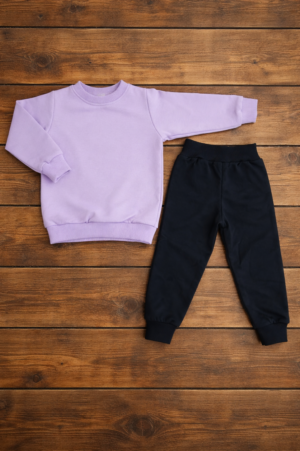 Conjunto de roupa infantil lilás e preta sobre fundo de madeira