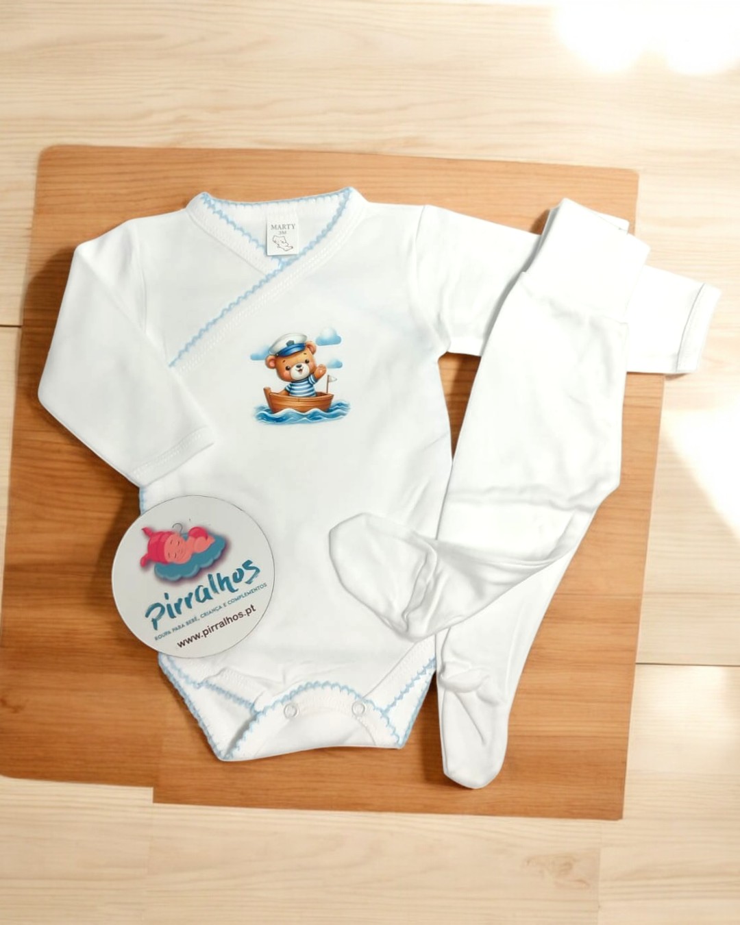 Conjunto de roupa de bebé branco com bordas azuis e estampa de ursinho num barco