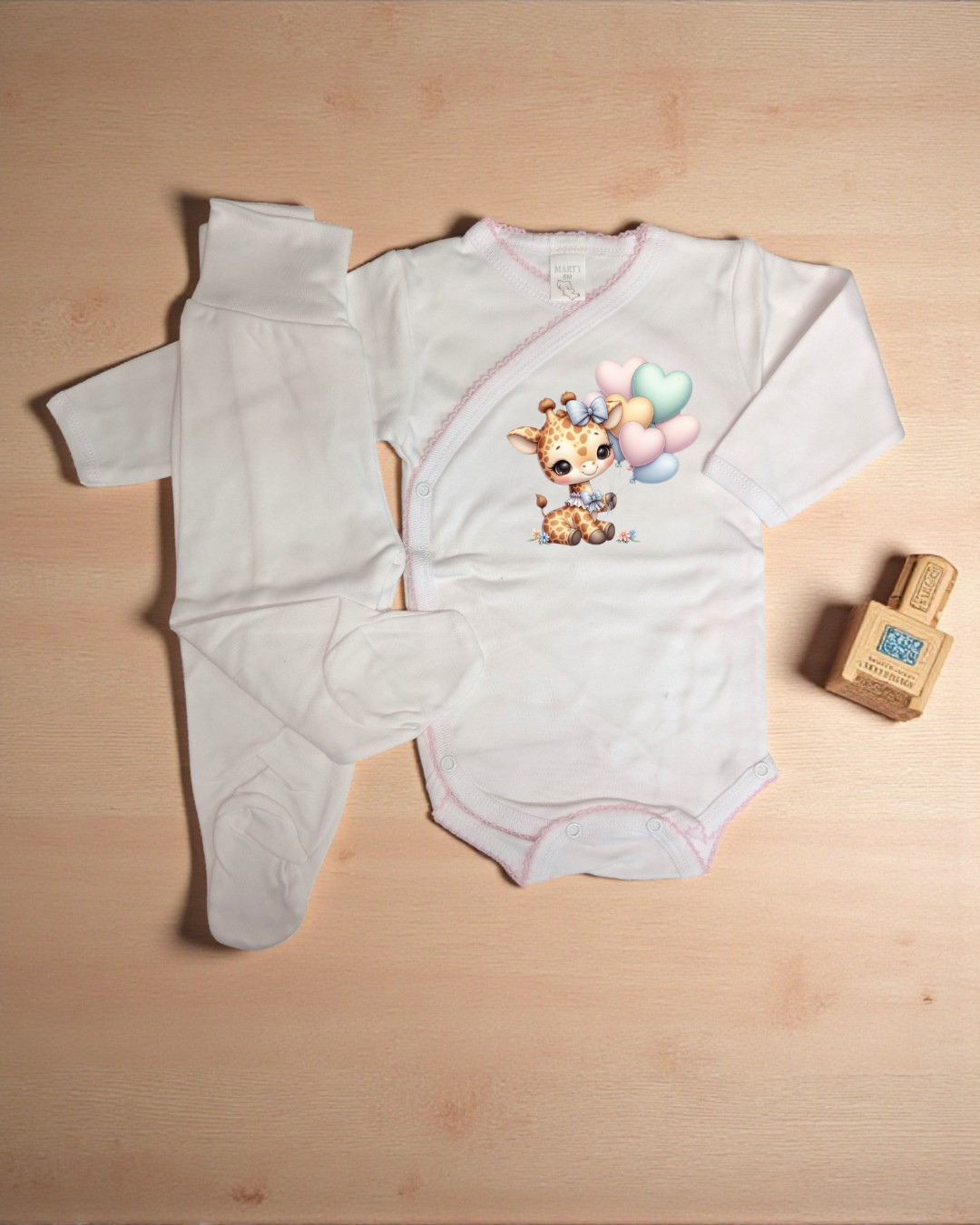 Conjunto branco de roupa de bebé com body estampado e calças de pé sobre superfície de madeira