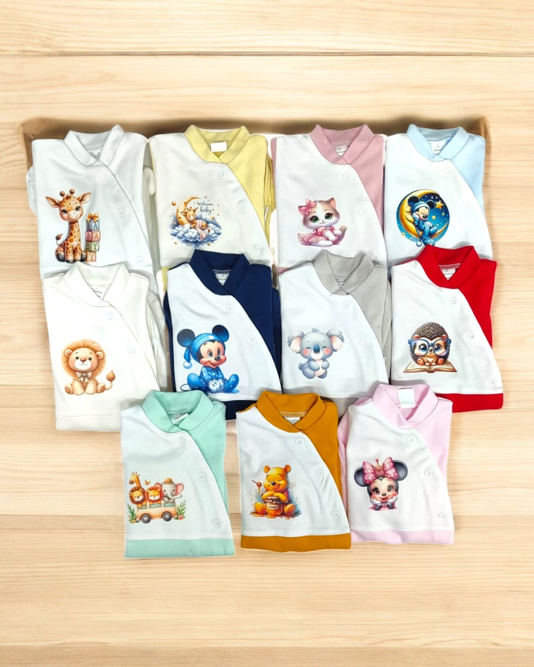 Conjunto de 11 peças de roupa de bebé com desenhos de animais e personagens em várias cores sobre madeira clara