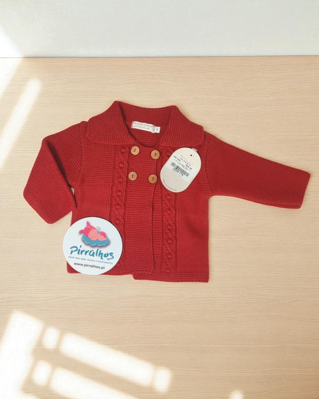Casaco vermelho de malha para bebé com botões de madeira e etiquetas visíveis