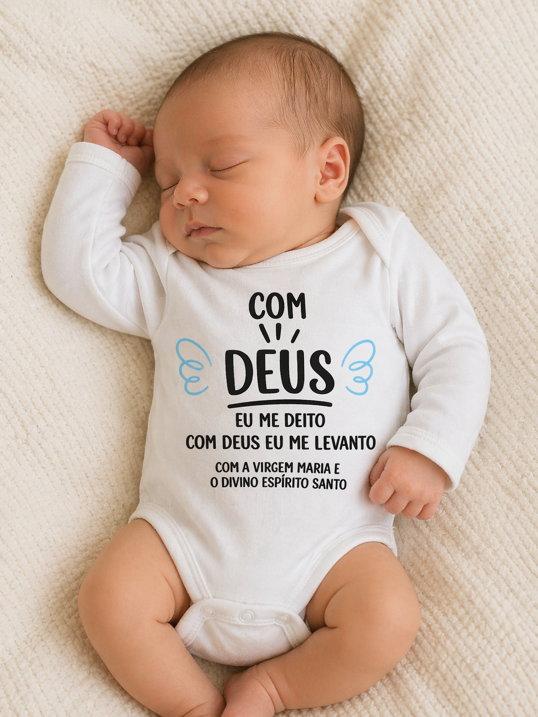 Body de bebé branco com texto religioso impresso, bebé adormecido deitado numa manta bege.