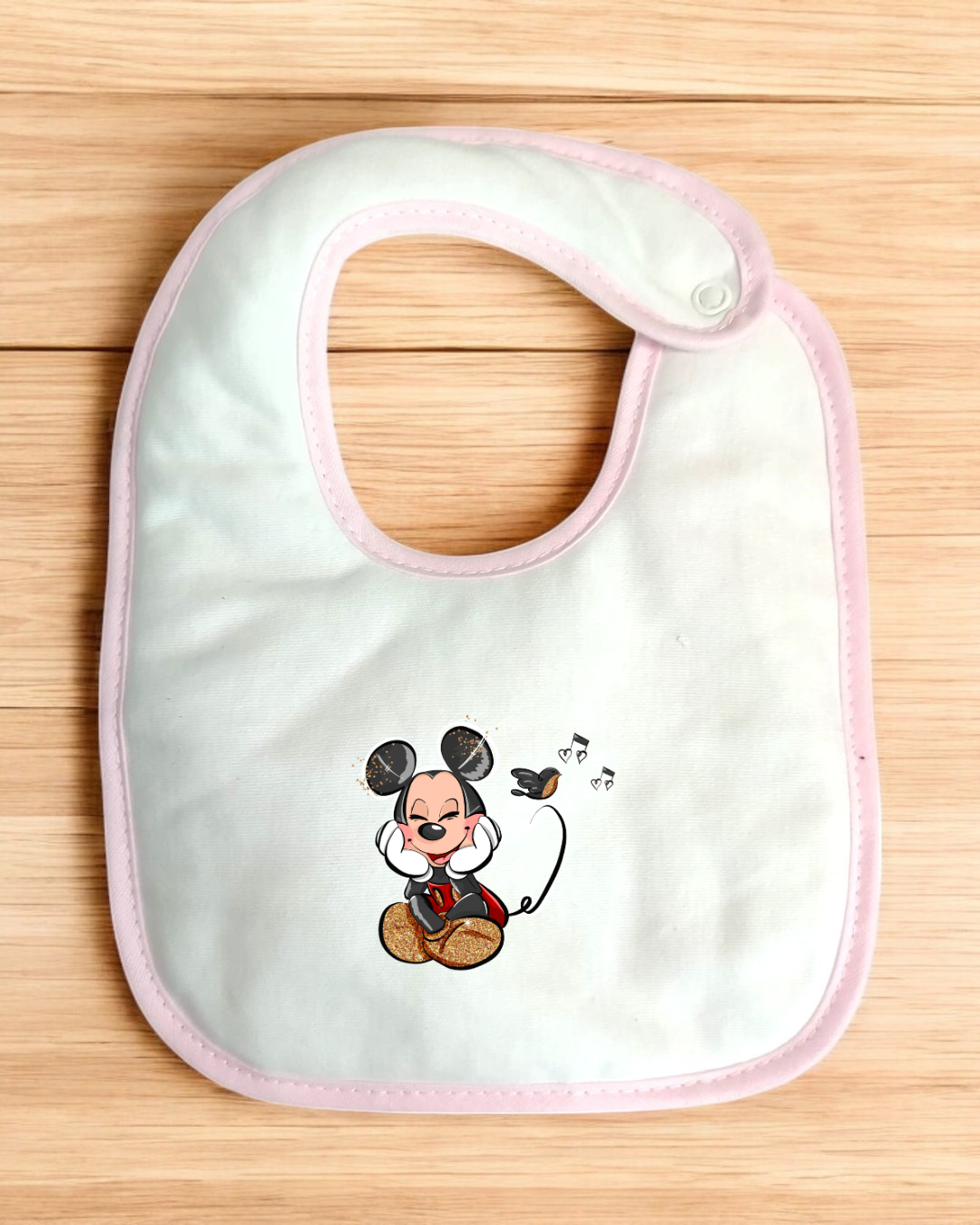 Babete branco com borda rosa e desenho do Mickey Mouse com um pássaro