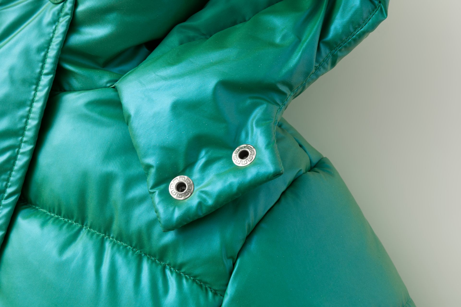 Detalhe de casaco acolchoado verde turquesa com ilhós metálicos