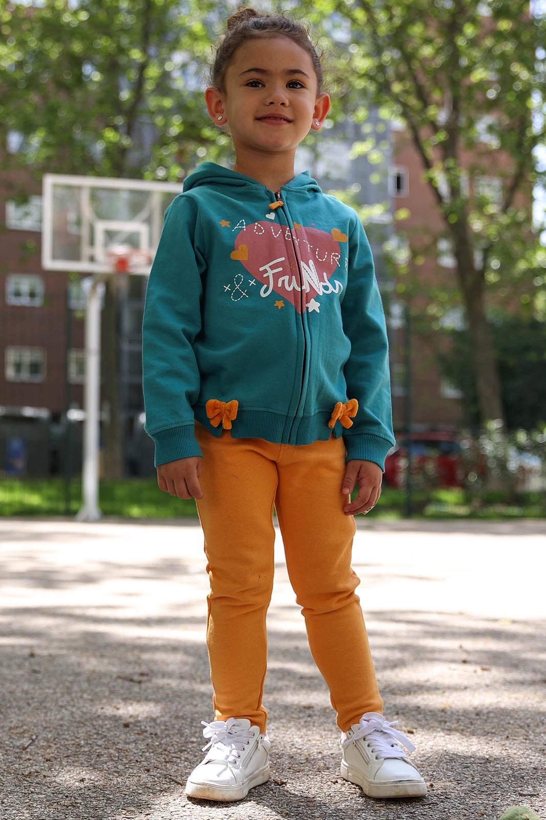 Criança com casaco azul turquesa e calças laranja em parque de basquetebol