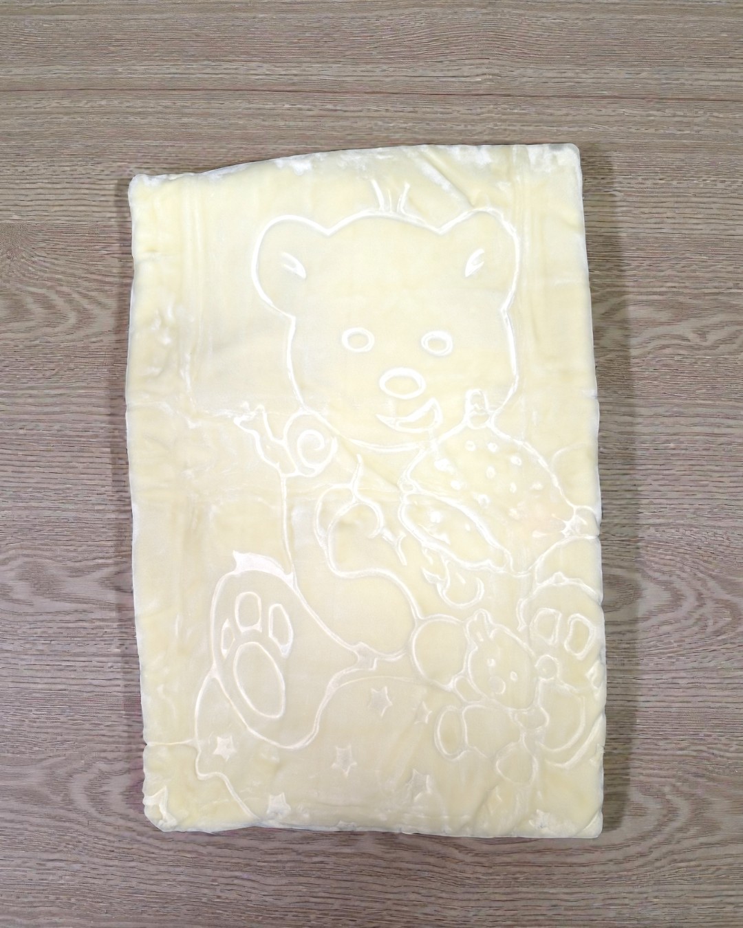 Manta amarela com desenho de urso gravado sobre superfície de madeira.