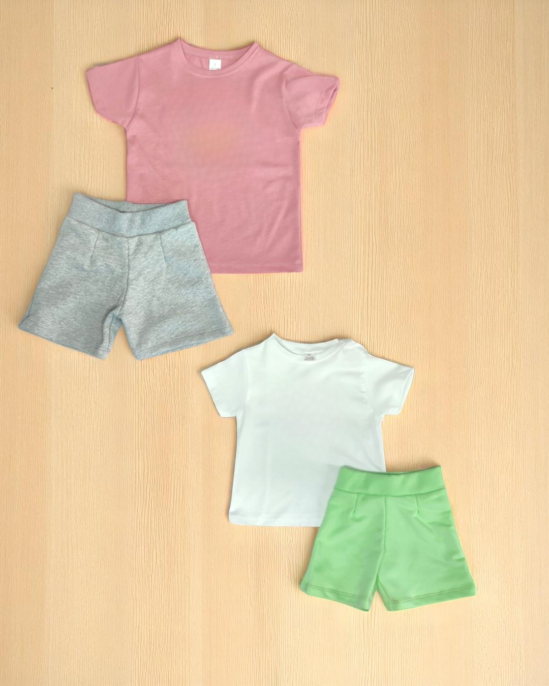 Conjunto infantil com duas t-shirts e dois pares de calções sobre fundo de madeira clara