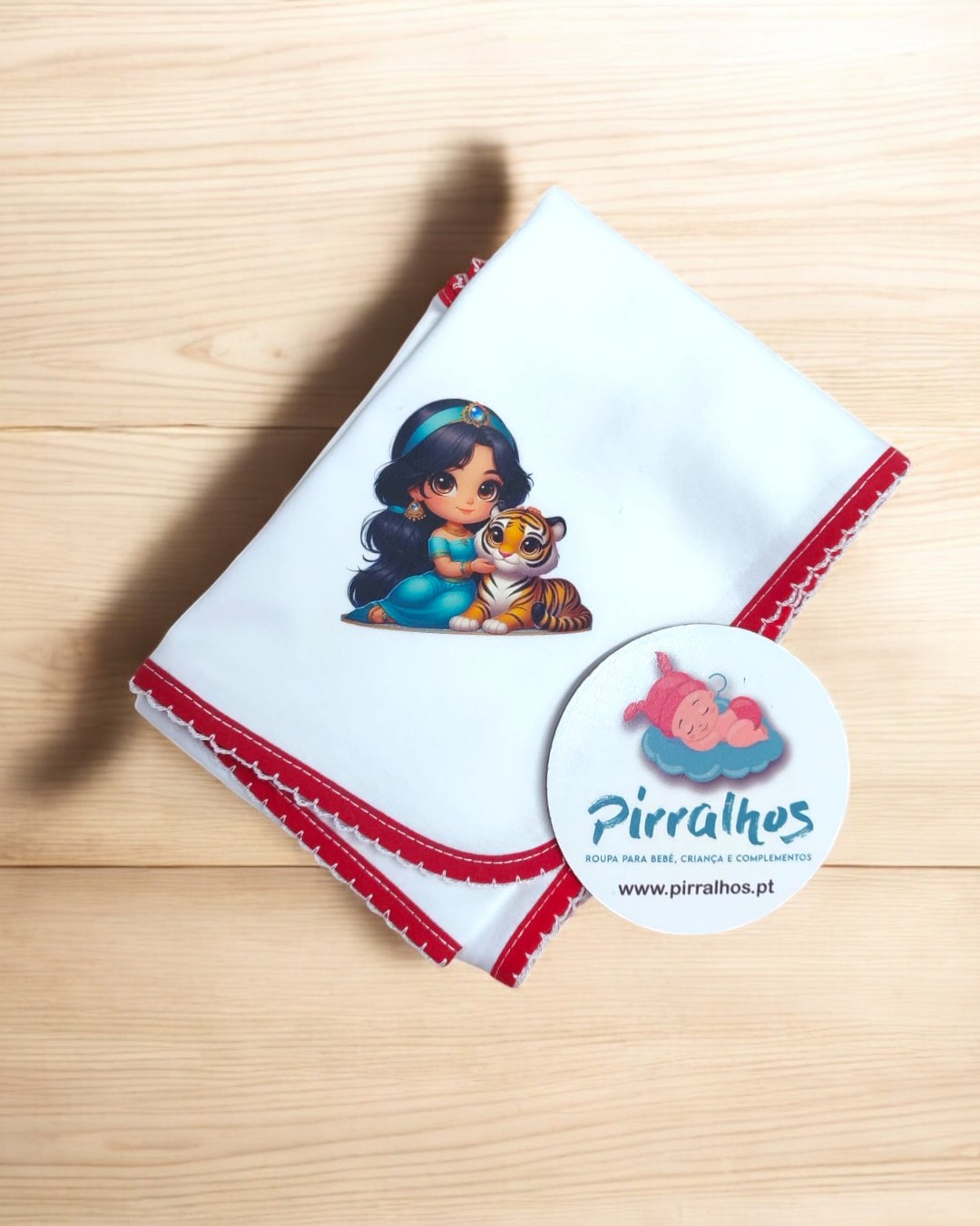 Fralda branca com personagem e borda vermelha e etiqueta redonda da marca Pirralhos