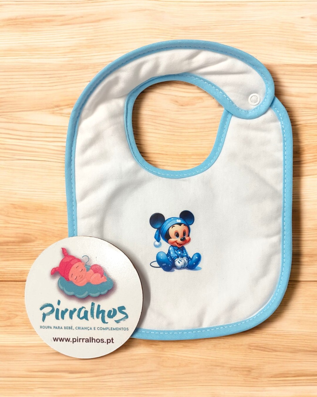 Babete de bebé branco com borda azul e Mickey Mouse azul, etiqueta da marca Pirralhos