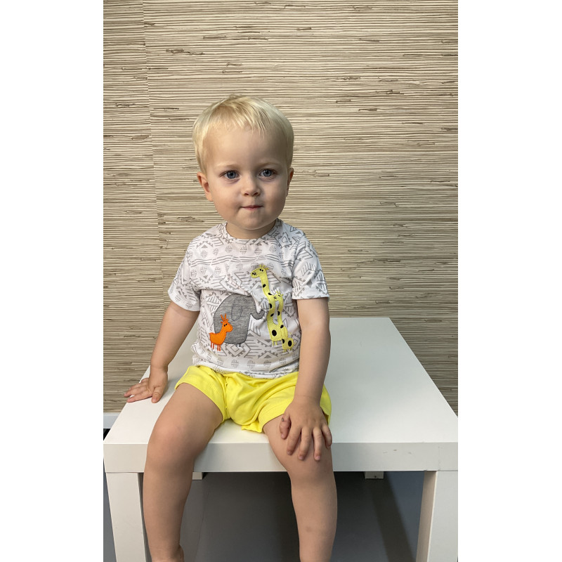 Criança com roupa infantil colorida sentada numa mesa branca com fundo texturado