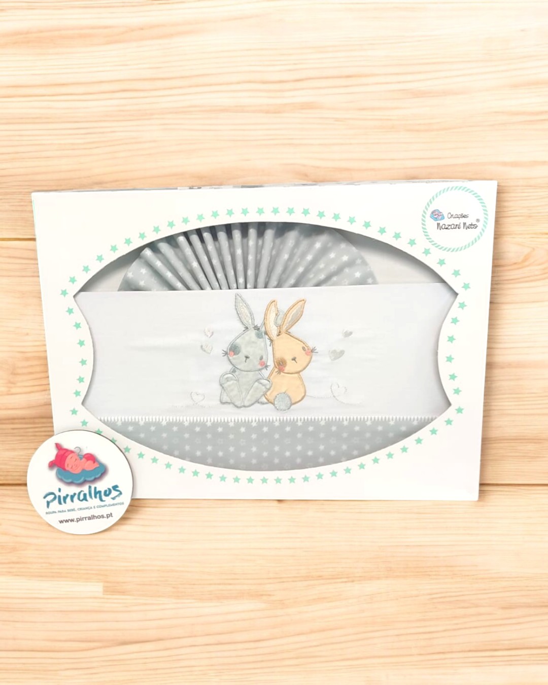 Fralda de bebé branca e cinza com bordado de coelhinhos em embalagem com estrelas verdes