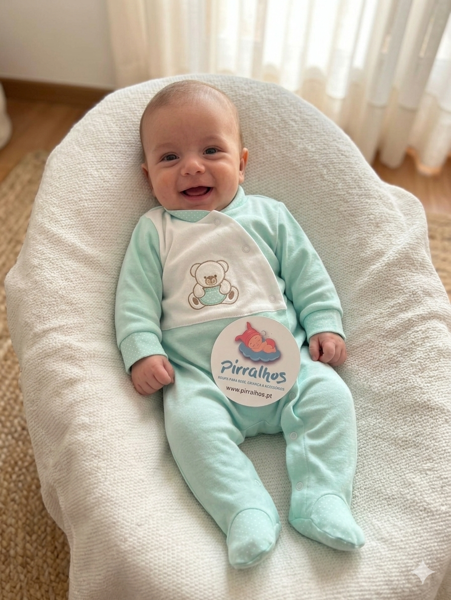 Bebé a sorrir de macacão verde claro com ursinho bordado, deitado em almofada branca